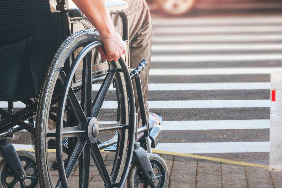 Foto com detalhe de pessoa cadeirante prestes a atravessar a faixa de uma rua.